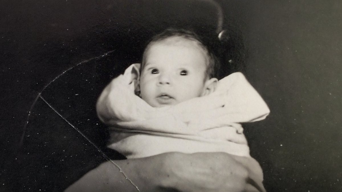 A baby held in someone's arms, black and white print with a crack across it