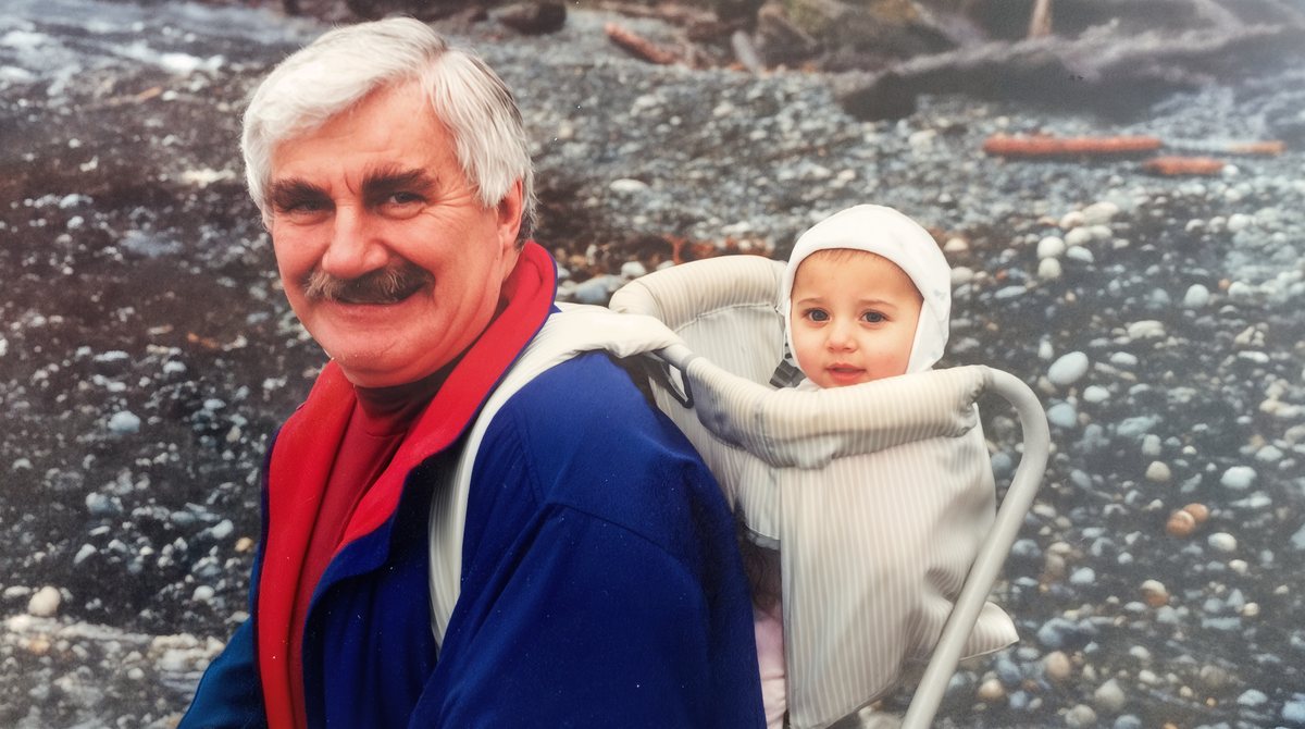 Peter Froud carrying Jessi in a backpack carrier on a stony beach